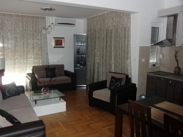 Wohnzimmer mit Küche in einer Wohnung in Budva, Montenegro: Polstermöbel, Glastisch, Parkett und moderne Ausstattung.