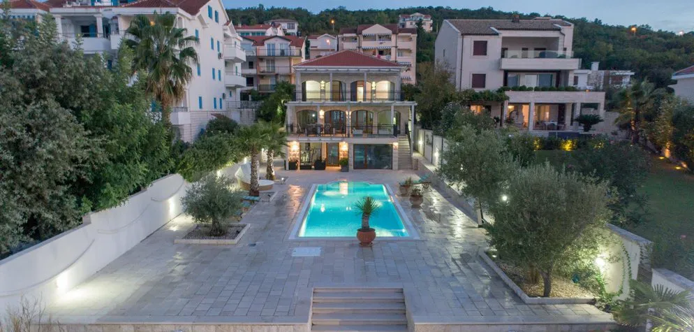 Three-story villa with a pool and terrace in Krašići, Montenegro: view of the house with lighting, a garden, and a lounge area.