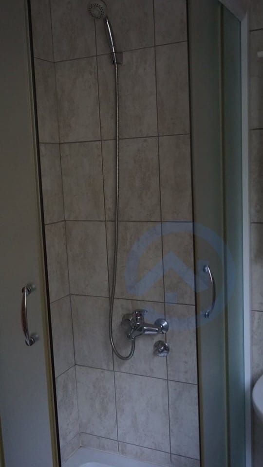 Tuš kabina sa bež pločicama u kupatilu kuće u Kavaču, Crna Gora. Moderna sanitarija i završna obrada.