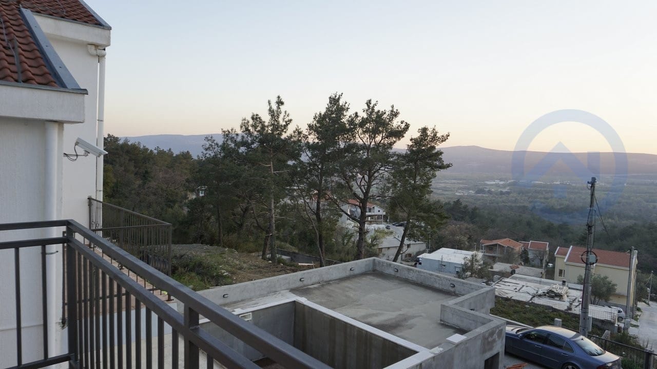 Pogled s balkona kuće u Kavaču, Crna Gora: panorama na planine, borovu šumu i susedne vile sa krovovima od crepova.