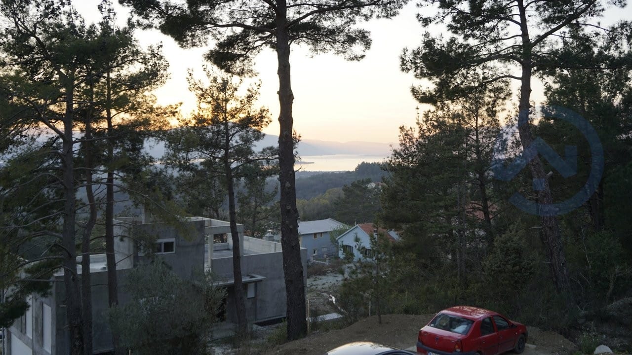 Pogled na more i borovu šumu iz kuće u Kavaču, Crna Gora: objekat u izgradnji i panoramski pejzaž pri zalasku sunca.