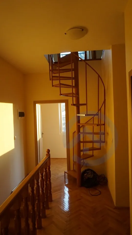 Spiral staircase in the interior of a house in Kavac, Montenegro: wooden parquet, classic railings, and light walls.