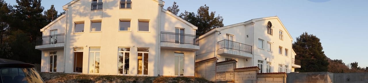 Bela trospratna kuća sa balkonima u Kavaču, Crna Gora: moderna fasada zgrade na pozadini borove šume.