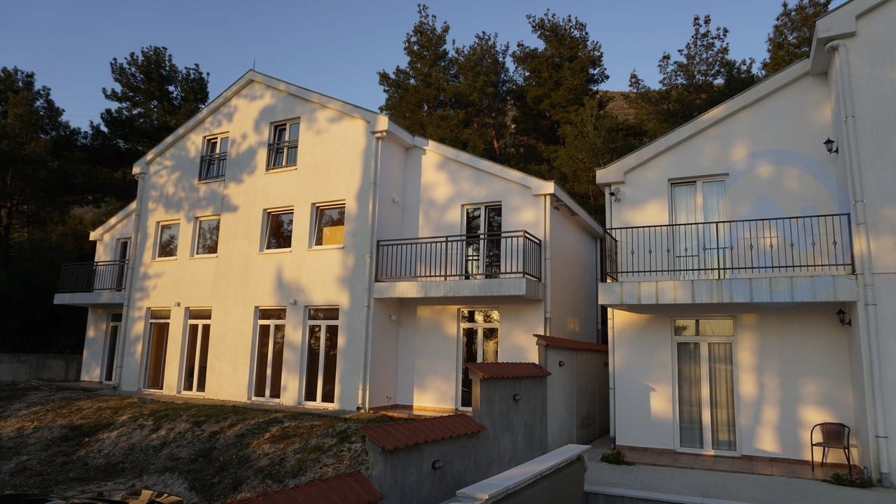 Bela moderna kuća sa balkonima i panoramskim prozorima u Kavaču, Crna Gora, okružena četinarskom šumom u zalazak sunca.
