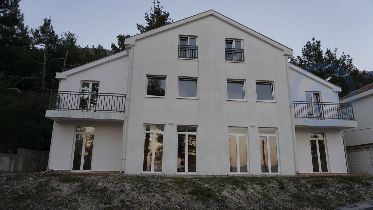Trospratna moderna kuća u Kavaču, Crna Gora: bela fasada, panoramski prozori i otvoreni balkoni sa ogradama.