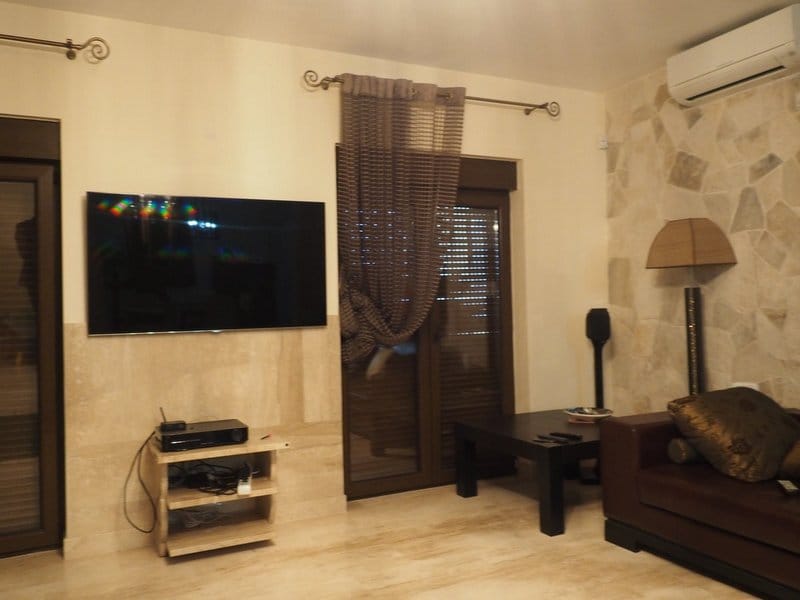 Dnevna soba vile u Stolivu, Crna Gora: kožna sofa, TV zona sa oblogom od prirodnog kamena i panoramski prozori.