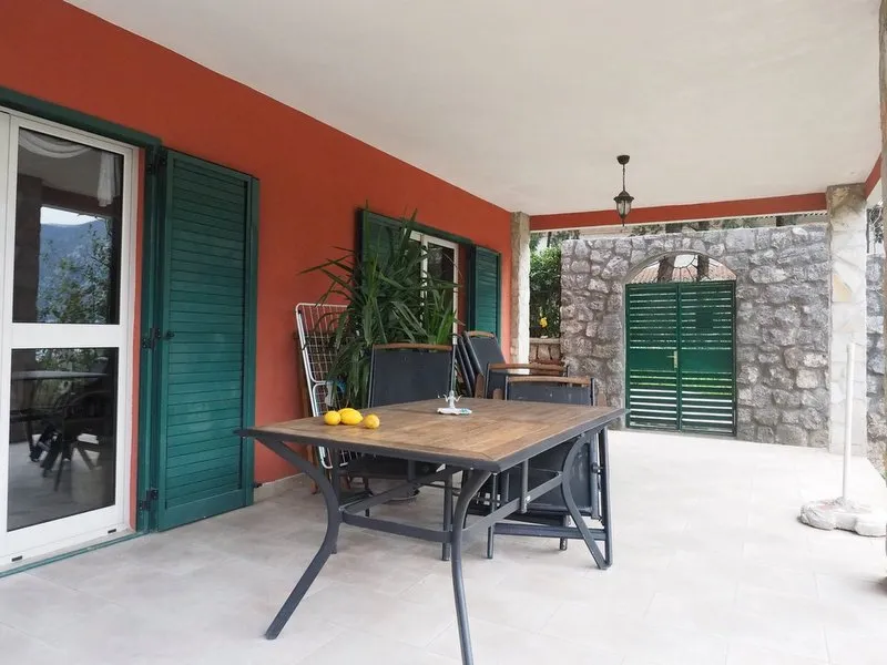 Geräumige Terrasse der Villa in Dobrota, Montenegro: Essbereich, Steinverkleidung, grüne Fensterläden und Bergblick.