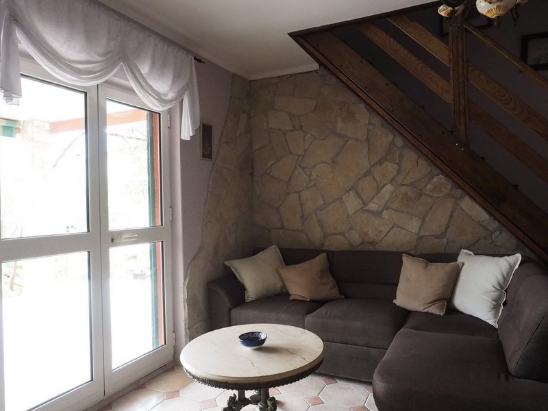 Wohnzimmer mit Steinverkleidung und Treppe in einer Villa in Dobrota, Montenegro: gemütliches Sofa und runder Tisch am Fenster.
