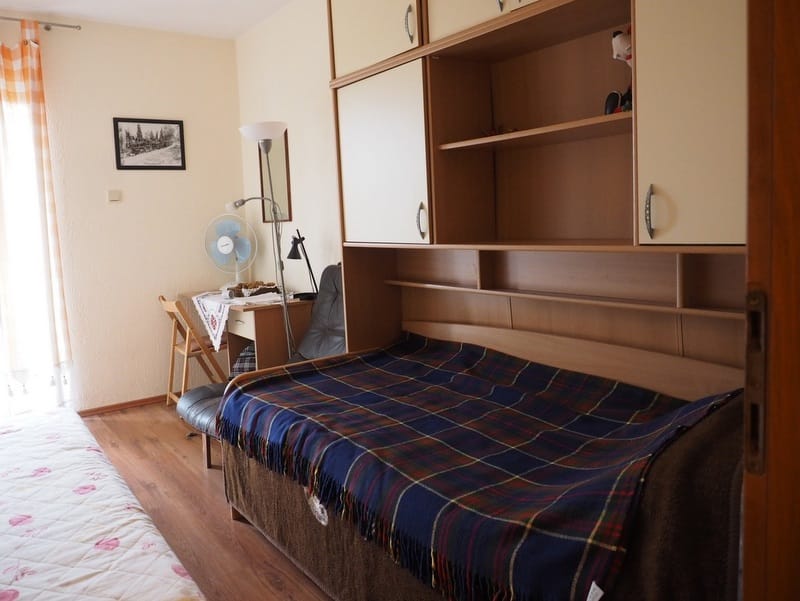Bedroom in a house in Đenovići, Montenegro: bed with a throw, built-in wardrobe, desk, and light wall finishes.