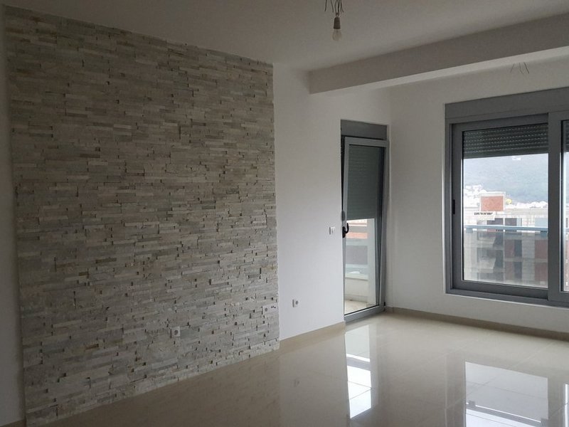 Helles Wohnzimmer in einer Wohnung in Dobrota, Montenegro: Akzentwand aus dekorativem Stein und Zugang zum Balkon.