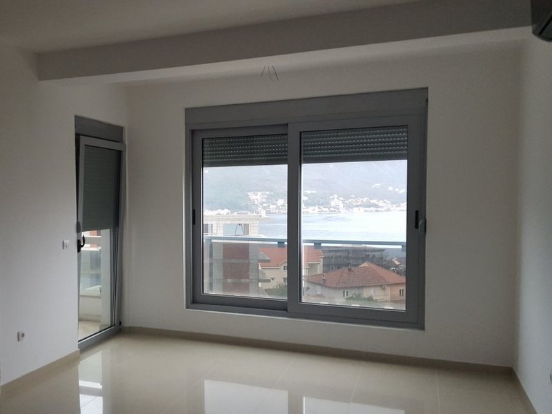 Helles Wohnzimmer in einer Wohnung in Dobrota, Montenegro, mit Panoramablick auf das Meer und die Berge durch große Fenster.