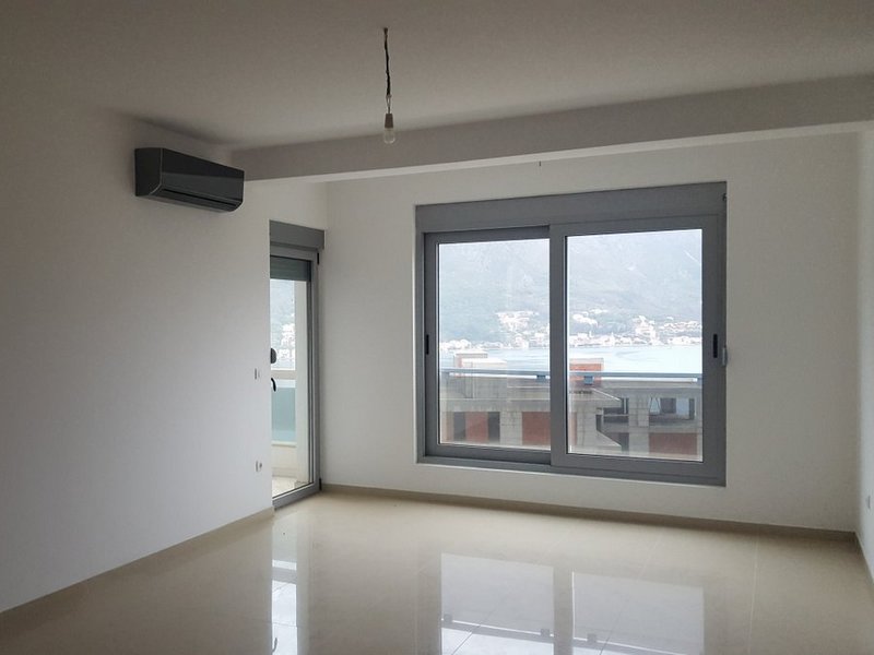 Helles Wohnzimmer in einer Wohnung in Dobrota, Montenegro: Panoramafenster mit Meerblick, Klimaanlage und Fliesenboden.