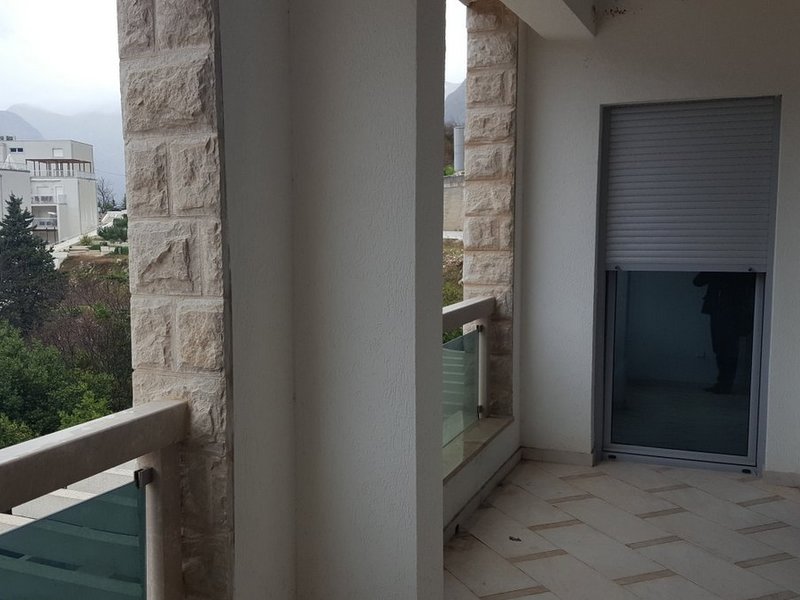 Balkon mit Steinverkleidung und Bergblick in einer Wohnung, Stadt Dobrota, Montenegro. Moderne Verglasung und Fliesen.
