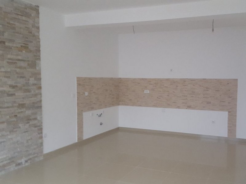 Küche in einer Wohnung in Dobrota, Montenegro: helle Wandverkleidung aus dekorativem Stein und Fliesenboden, Bereich für die Küchenzeile.