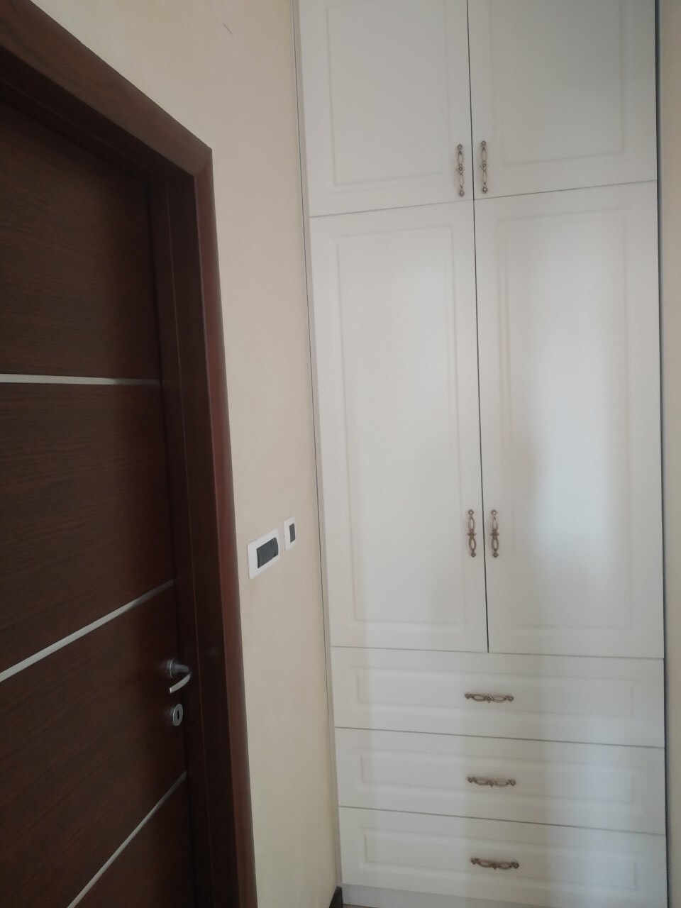 Ugradni beli ormar sa fiokama u spavaćoj sobi stana u Budvi, Crna Gora, pored tamnih unutrašnjih vrata.