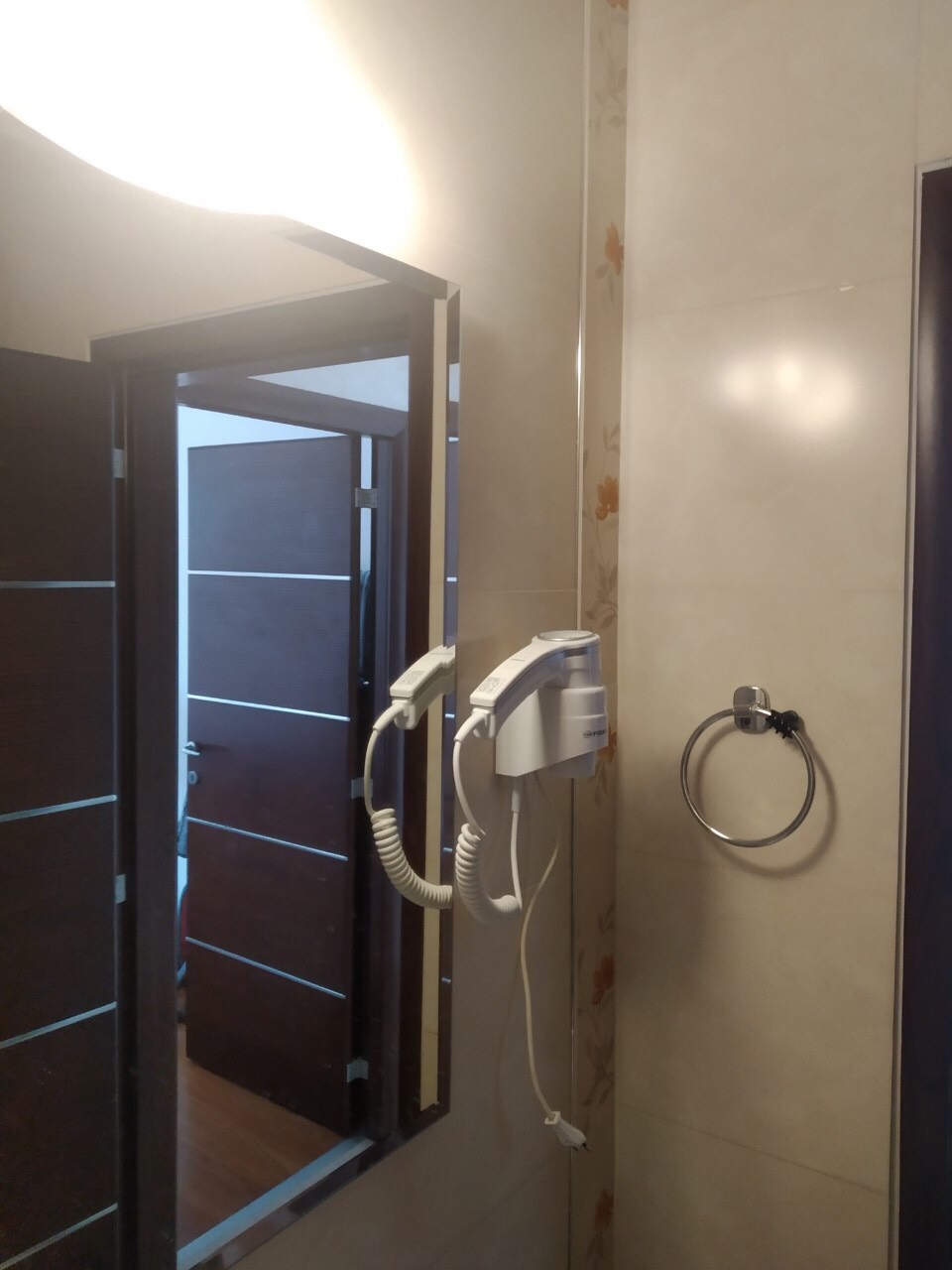 Kupatilo u stanu u Budvi, Crna Gora: ogledalo, zidni fen i držač za peškire na svetlim pločicama.