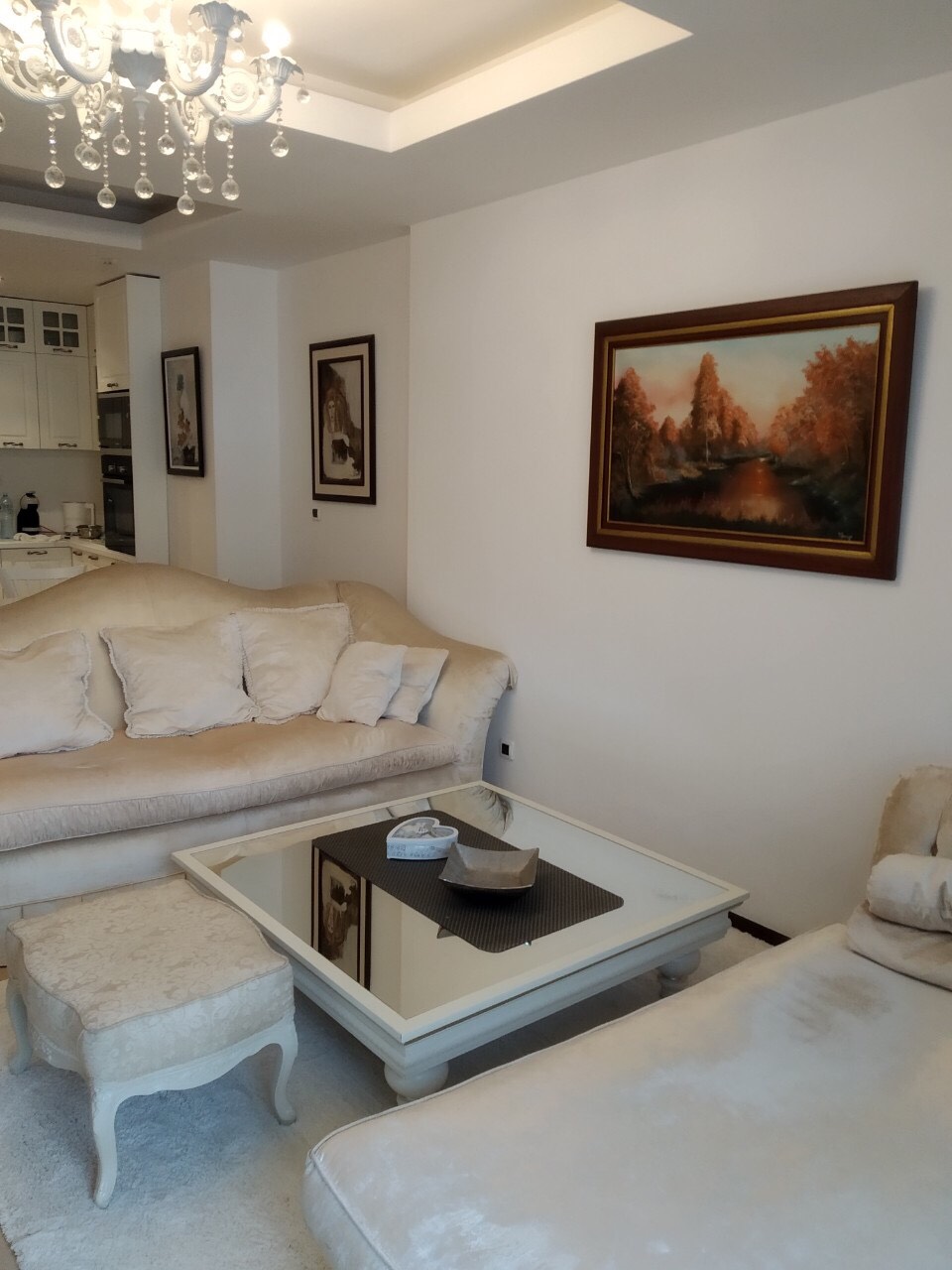 Svetla dnevna soba u stanu u Budvi, Crna Gora: bež sofa, ogledni klub sto i luster u enterijeru.