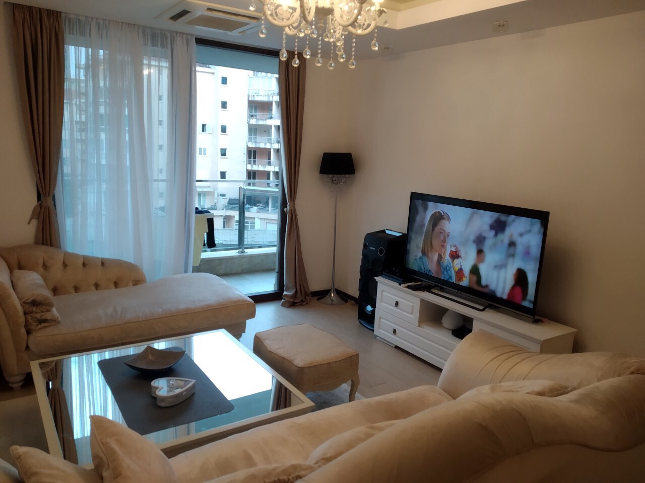 Udoban dnevni boravak u stanu u Budvi, Crna Gora: bež meblirana garnitura, stakleni sto i izlaz na balkon.