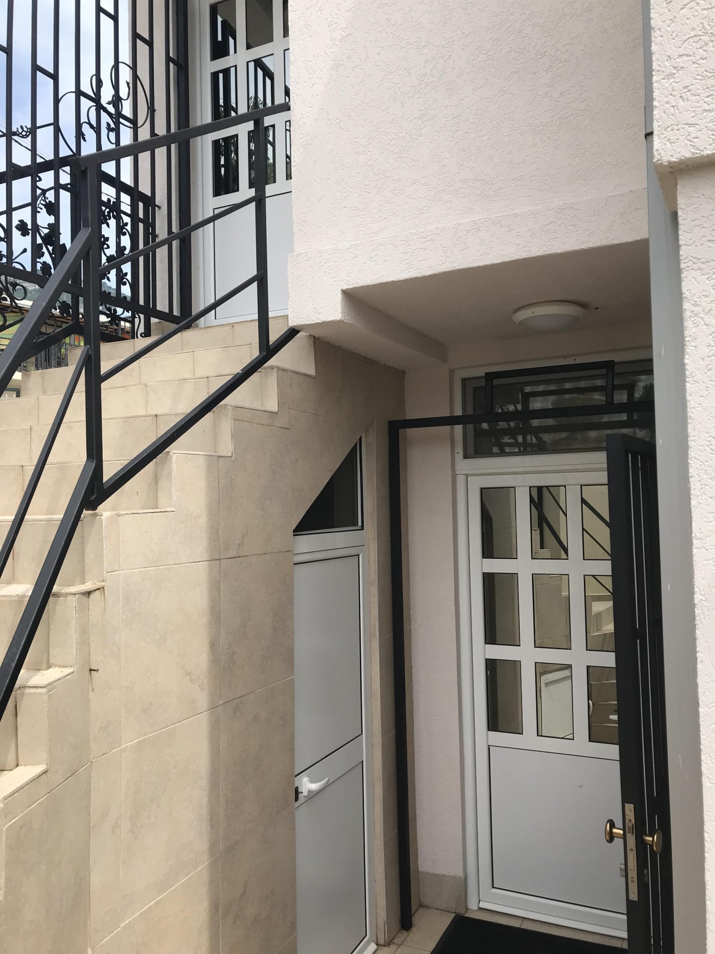 Eingang zum Haus in Bar, Montenegro: weiße Treppe mit schmiedeeisernem Geländer und moderne Kunststofftüren mit Verglasung.