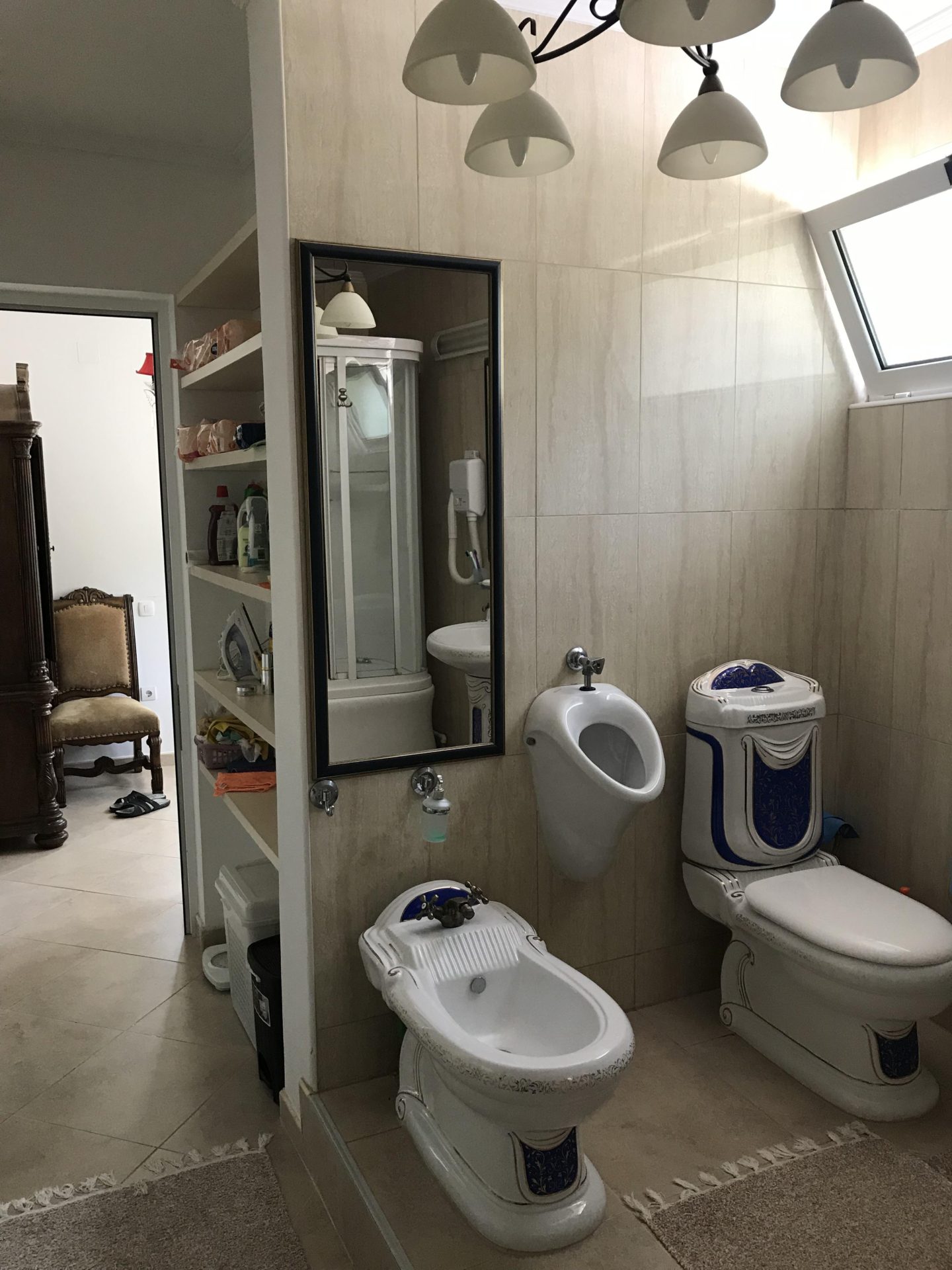 Badezimmer mit Bidet, Toilette und Urinal in einem Haus in Bar, Montenegro, mit heller Fliesenverkleidung.