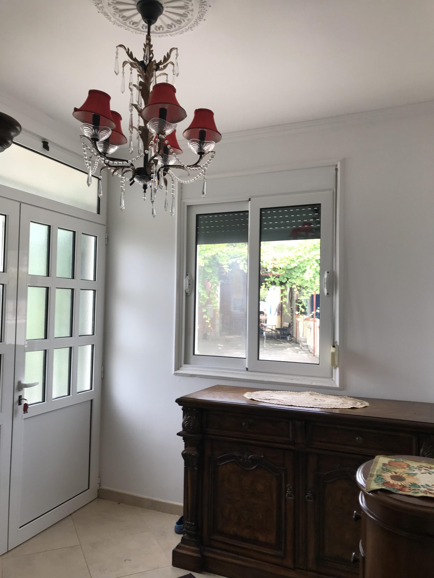 Wohnzimmer in einem Haus in Bar, Montenegro: antike Kommode, klassische Kronleuchter mit roten Lampenschirmen und Blick auf den Garten.