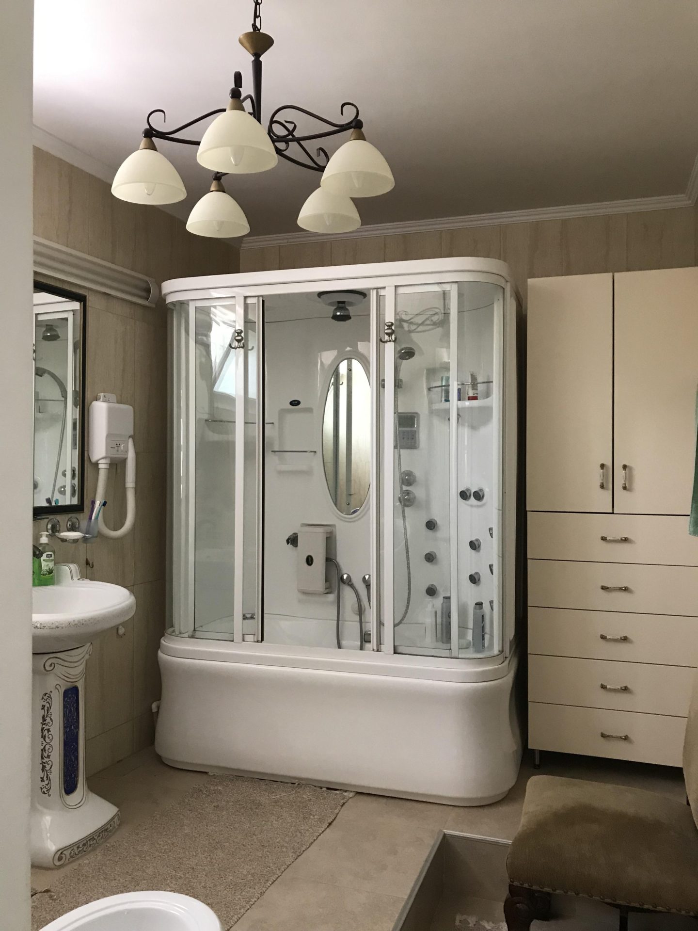 Badezimmer in einem Haus in Bar, Montenegro: Duschkabine mit Hydromassage, helle Möbel und klassischer Kronleuchter.