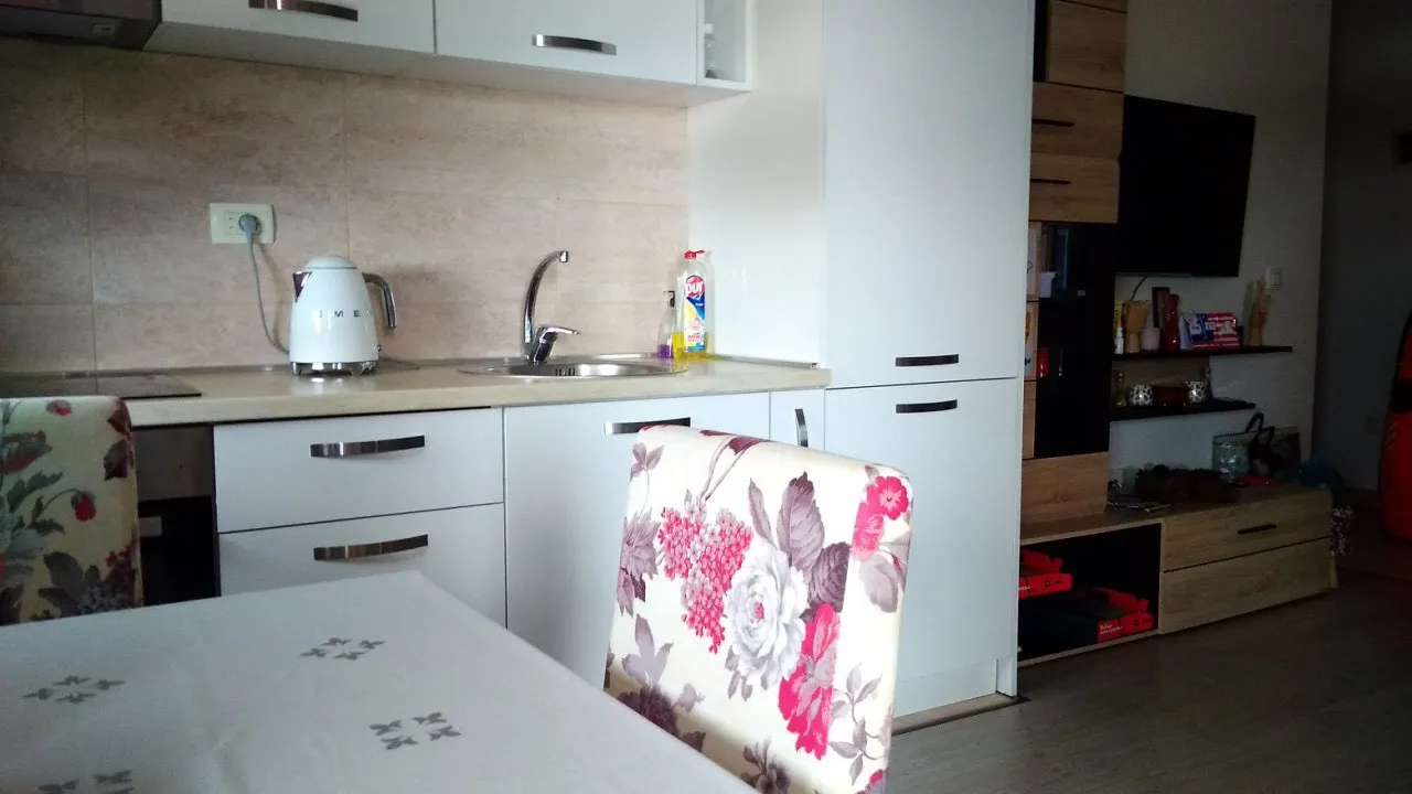 Savremena kuhinja u stanu u Budvi, Crna Gora: beli frontovi, trpezarijski deo sa stolicama s cvetnim dezenom i TV zona.