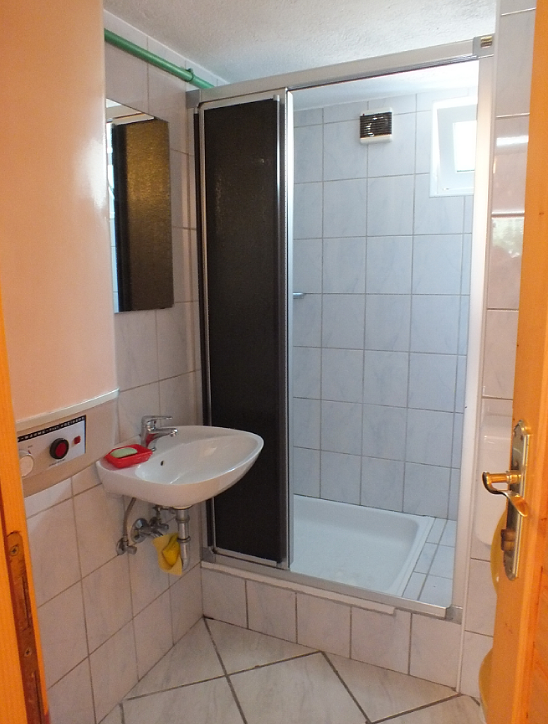 Salle de bains dans une maison à Bar, Monténégro : cabine de douche, lavabo, carrelage clair et chauffe-eau.