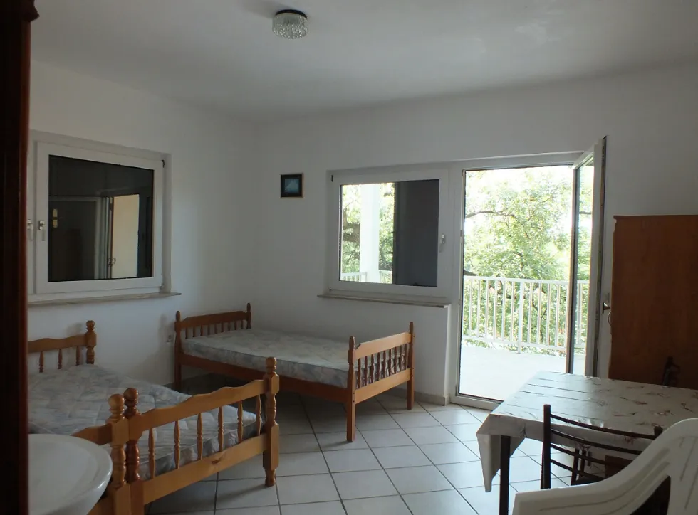 Helles Schlafzimmer mit zwei Holzbetten und Zugang zur Terrasse in einem Haus, Stadt Bar, Montenegro.