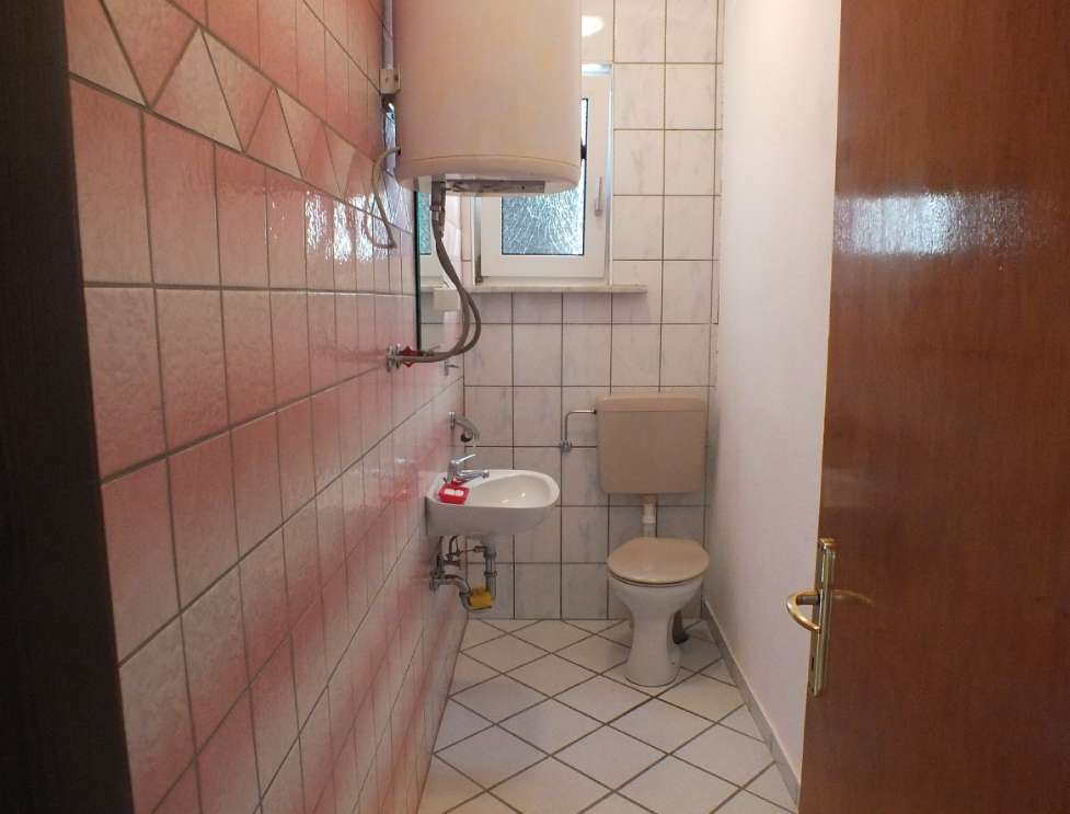 Salle de bains avec carrelage rose, chauffe-eau et fenêtre dans une maison à vendre, ville de Bar, Monténégro.