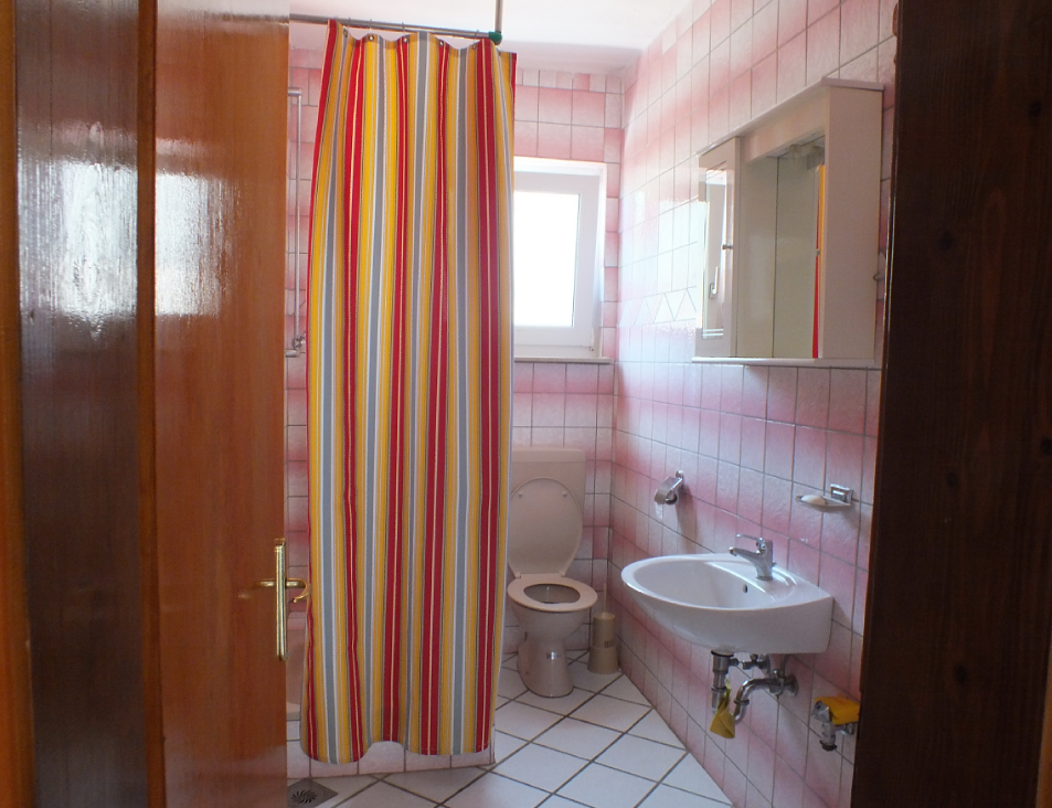 Salle de bain dans une maison à Bar, Monténégro : carrelage clair, espace douche avec rideau coloré, lavabo et toilettes.