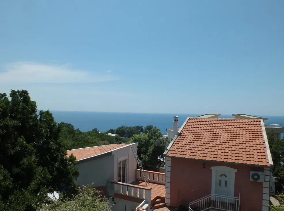 Blick auf das Meer und die Terrasse des Hauses mit Ziegeldach in Bar, Montenegro, umgeben von Grün und Bäumen.