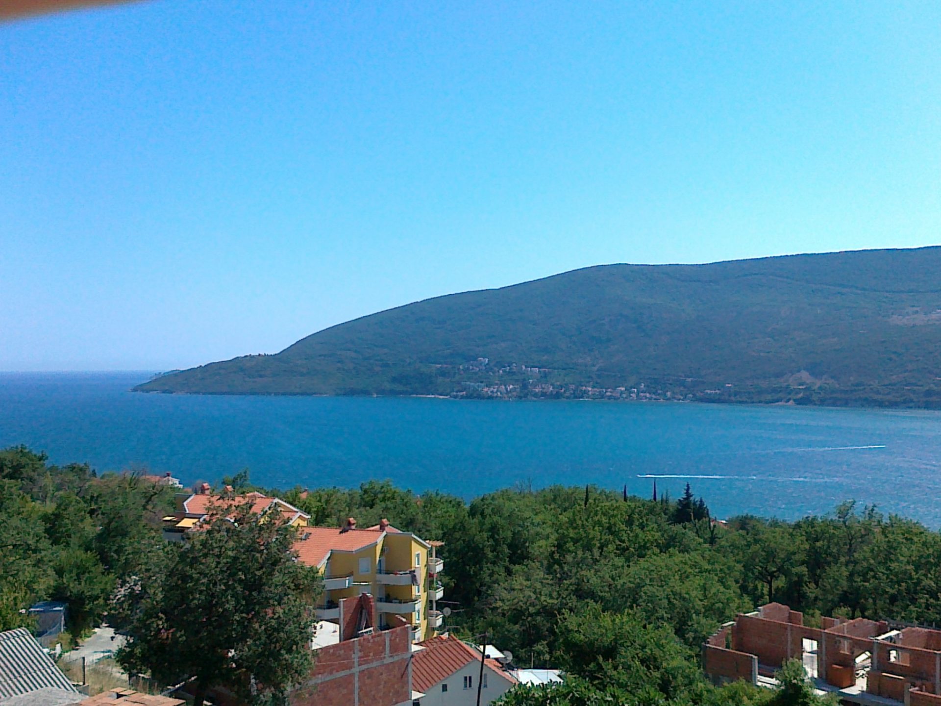 Karadağ, Herceg Novi’deki evden deniz ve dağların panoramik manzarası: yeşil tepeler, kıyı şeridi ve konut yapıları.