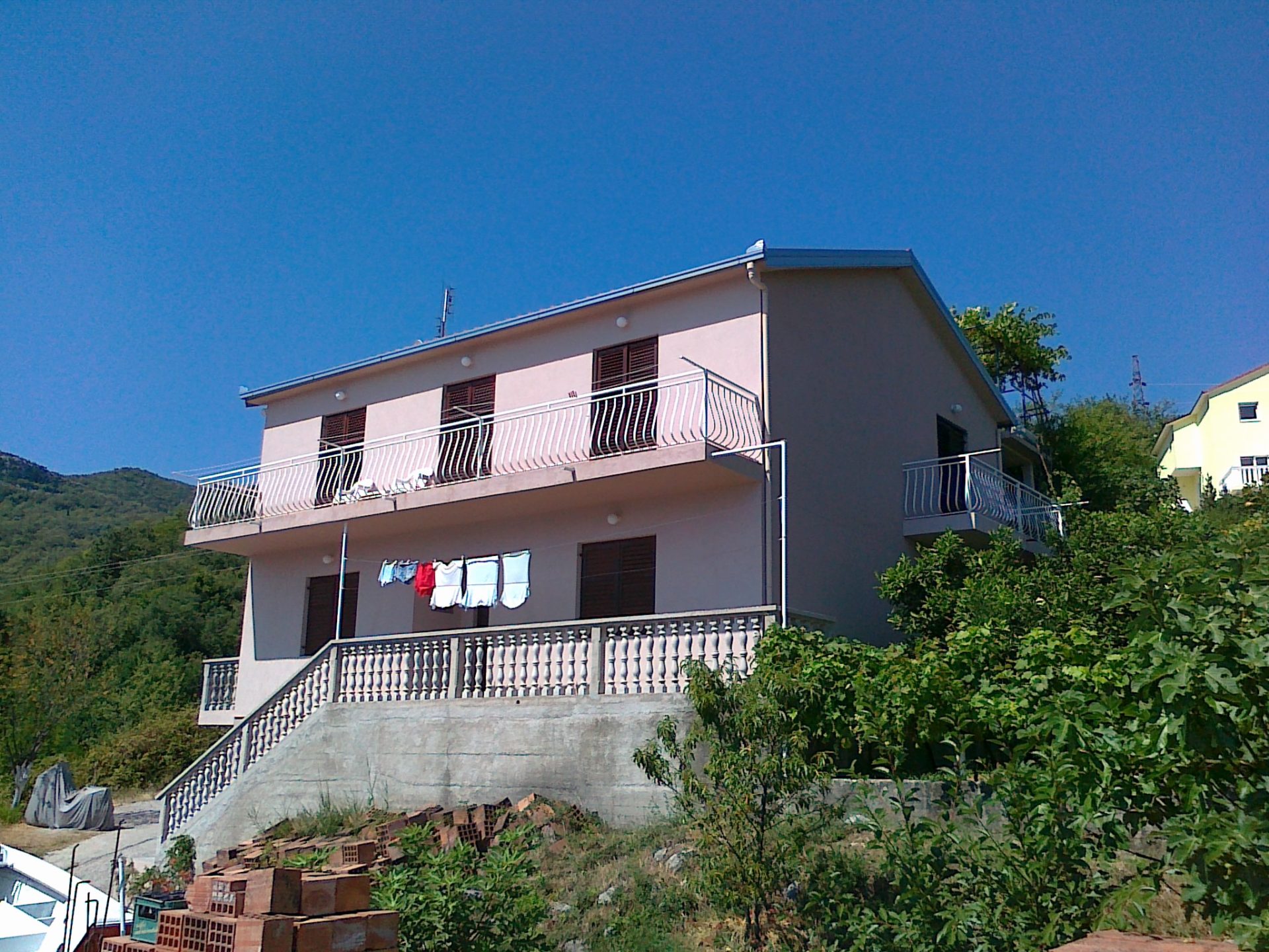 Karadağ, Herceg Novi’de teraslı ve korkuluklu iki katlı ev, cephe ve yeşil arsa görünümü.
