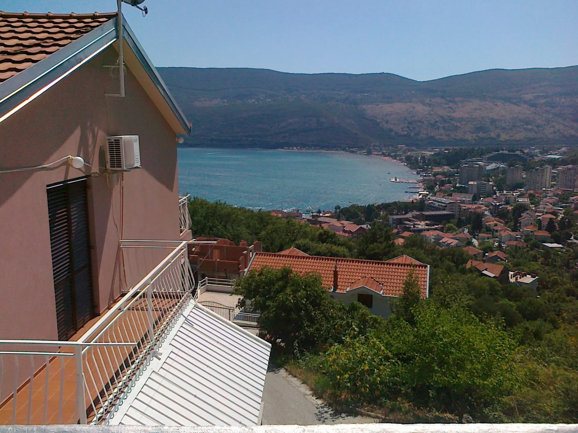 View from a balcony overlooking the sea and town. House exterior with AC unit visible.