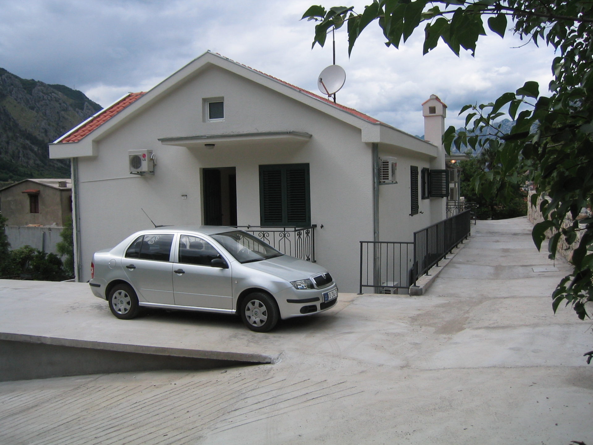 Weißes Einfamilienhaus mit Ziegeldach und Parkplatz in Kotor, Montenegro: Außenansicht der Fassade mit Klimaanlage.