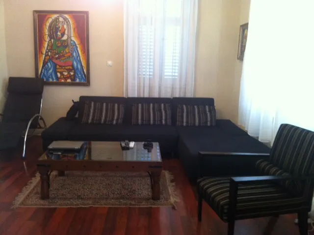 Living room with dark sectional sofa, wooden coffee table, and colorful painting on the wall.