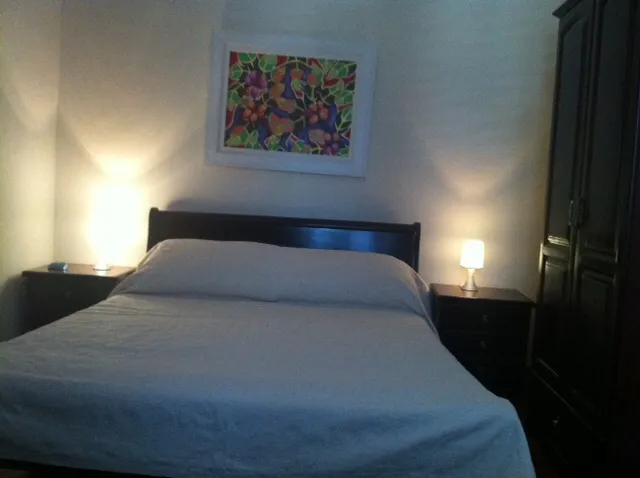 Bedroom featuring a double bed with dark headboard, nightstands with lamps, and a tall wardrobe on the right.