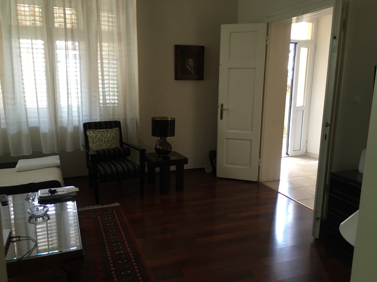 Wohnzimmer in einem Haus in Herceg Novi, Montenegro: dunkles Parkett, ein gestreifter Sessel, ein Couchtisch und Zugang zur Terrasse.
