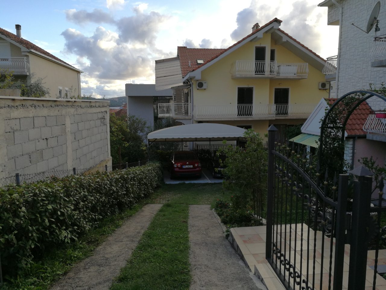 Zweistöckiges Haus in Tivat, Montenegro, mit privatem überdachten Parkplatz, grünem Grundstück und schmiedeeisernem Tor.
