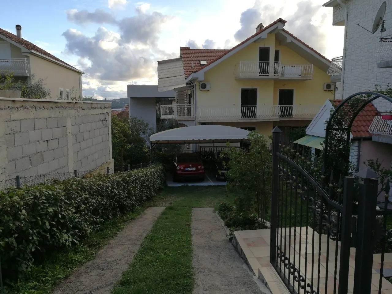 Zweistöckiges Haus in Tivat, Montenegro, mit privatem überdachten Parkplatz, grünem Grundstück und schmiedeeisernem Tor.