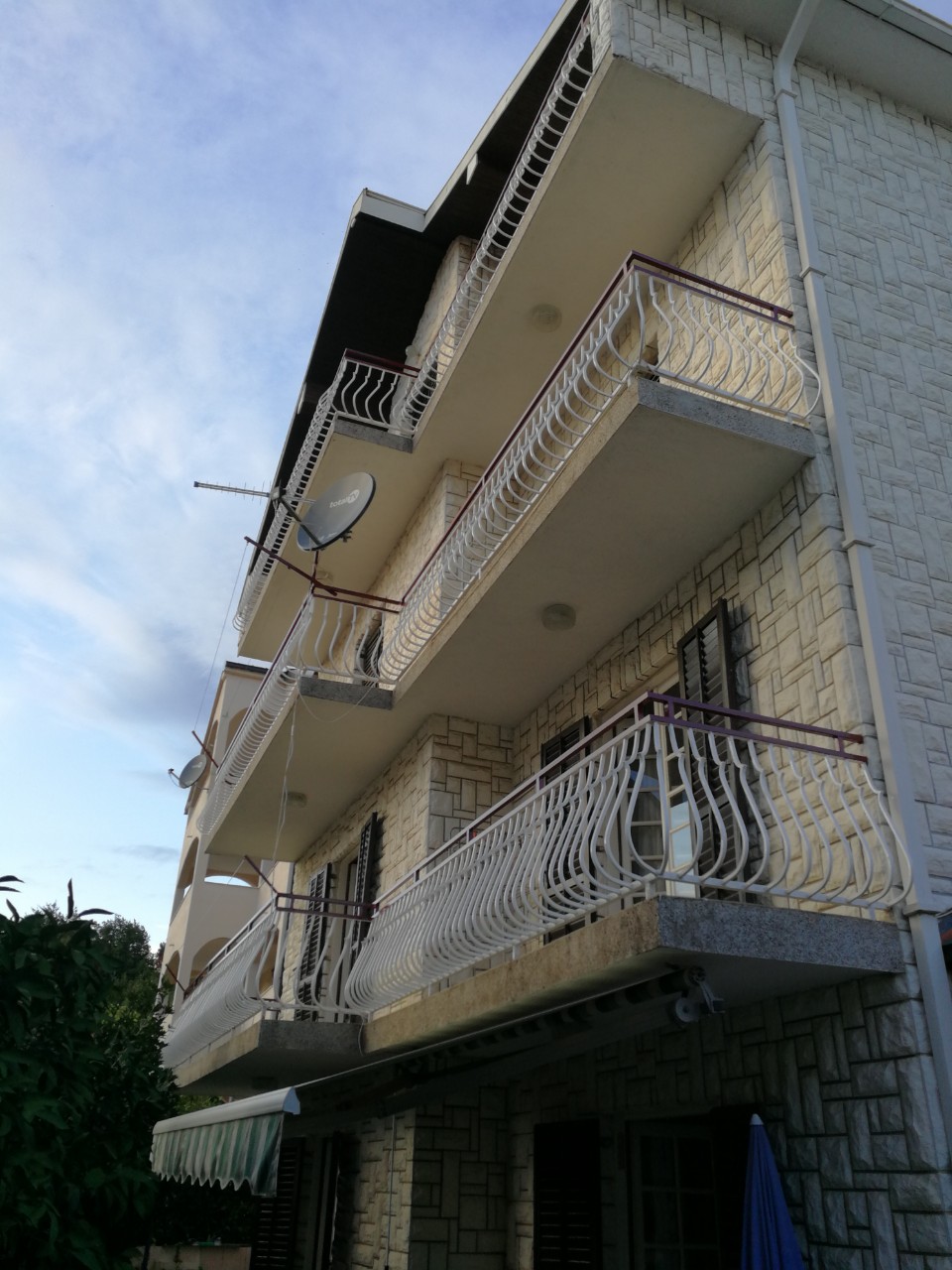 Fassade eines dreistöckigen Hauses in Tivat, Montenegro, mit Steinverkleidung und schmiedeeisernen Balkonen auf jeder Etage.