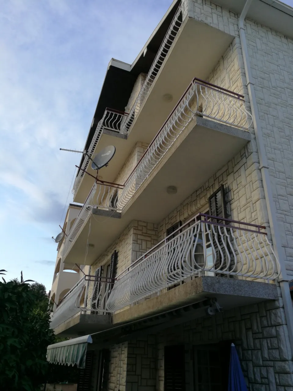 Fassade eines dreistöckigen Hauses in Tivat, Montenegro, mit Steinverkleidung und schmiedeeisernen Balkonen auf jeder Etage.