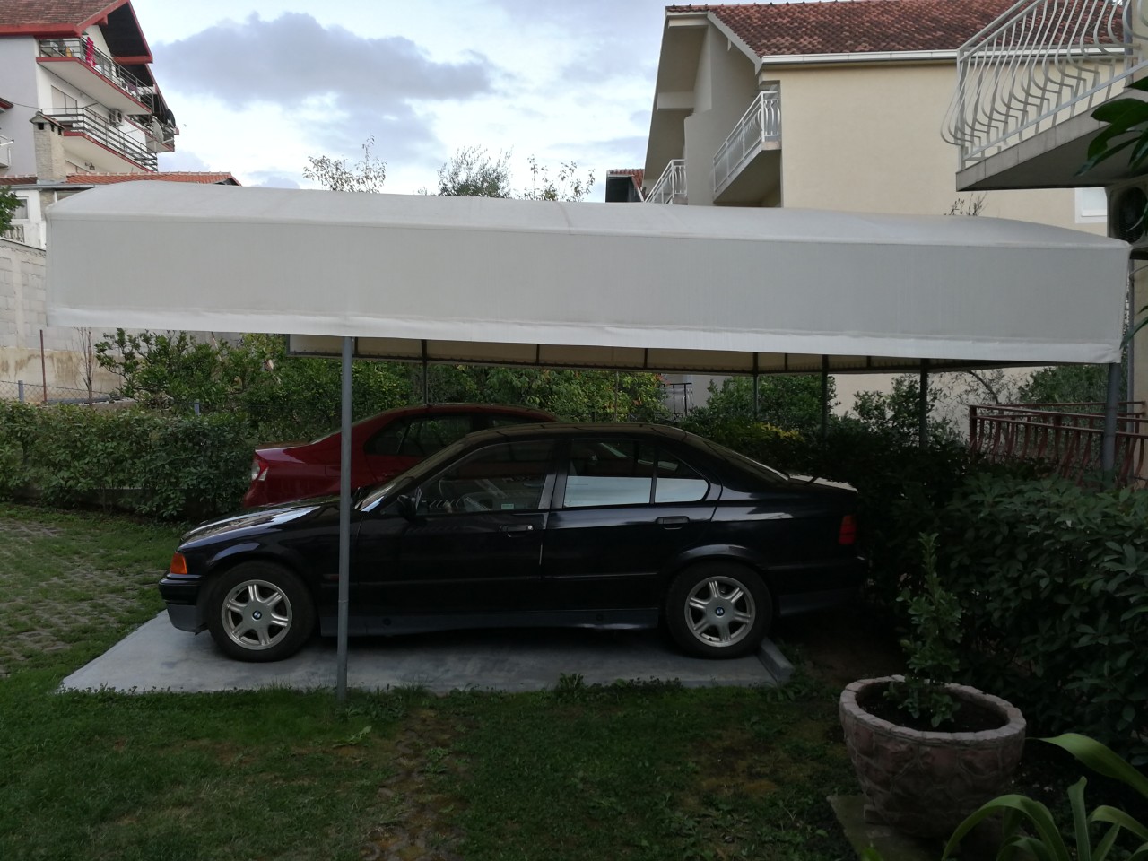 Überdachter Parkplatz für Autos auf dem Privatgrundstück eines Hauses in Tivat, Montenegro, mit grünem Garten und Überdachung.