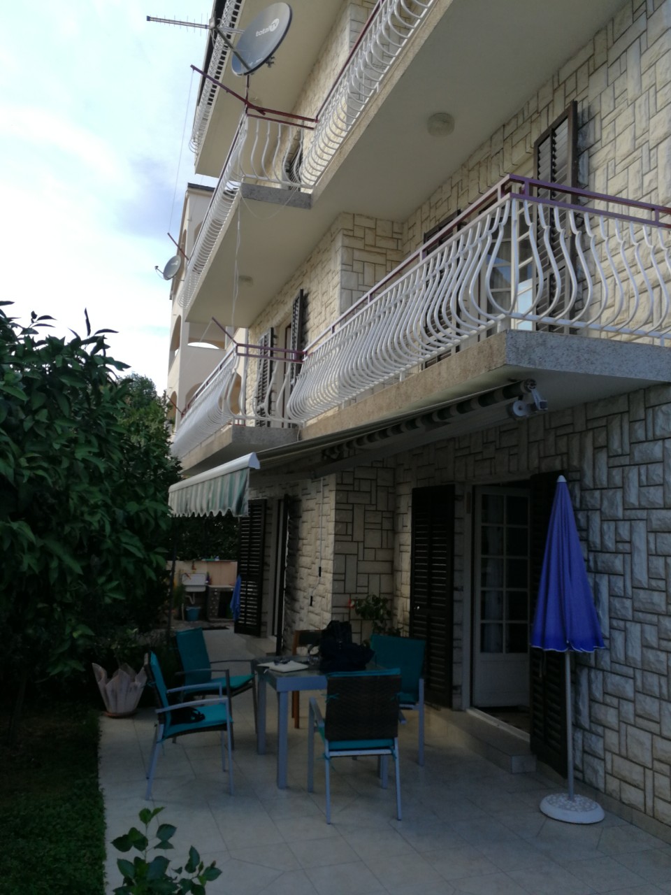 Fassade eines Hauses in Tivat, Montenegro: Steinverkleidung, Balkone mit schmiedeeisernen Geländern und eine Terrasse mit Loungemöbeln.