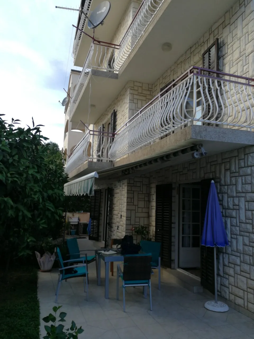 Fassade eines Hauses in Tivat, Montenegro: Steinverkleidung, Balkone mit schmiedeeisernen Geländern und eine Terrasse mit Loungemöbeln.