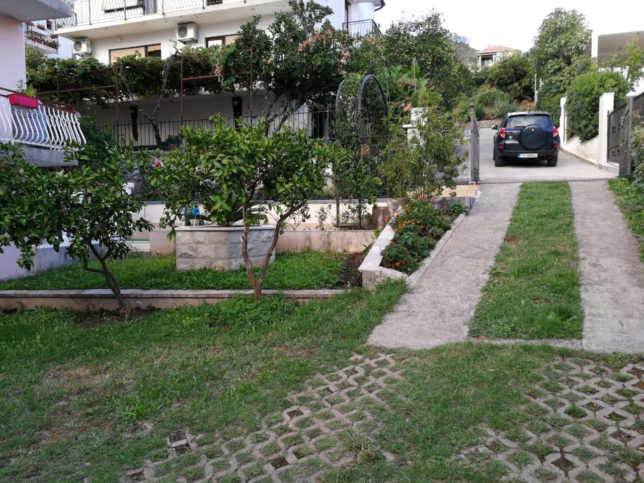 Innenhof eines Privathauses in Tivat, Montenegro: grüner Garten, Parkplatz und Blick auf die Fassade des Gebäudes.
