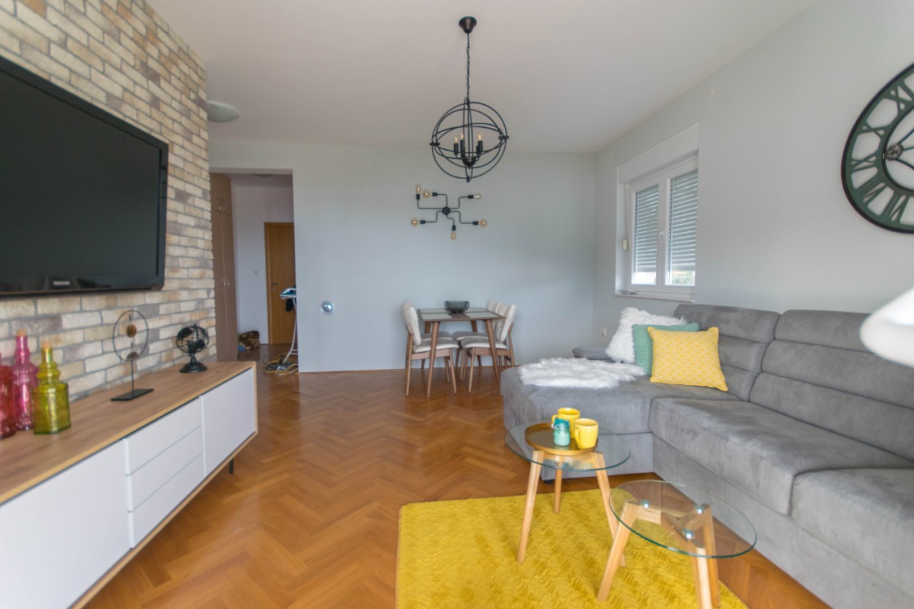 Modernes Wohnzimmer in einer Wohnung in Herceg Novi, Montenegro: Ziegelwand, graues Sofa und Parkettboden.