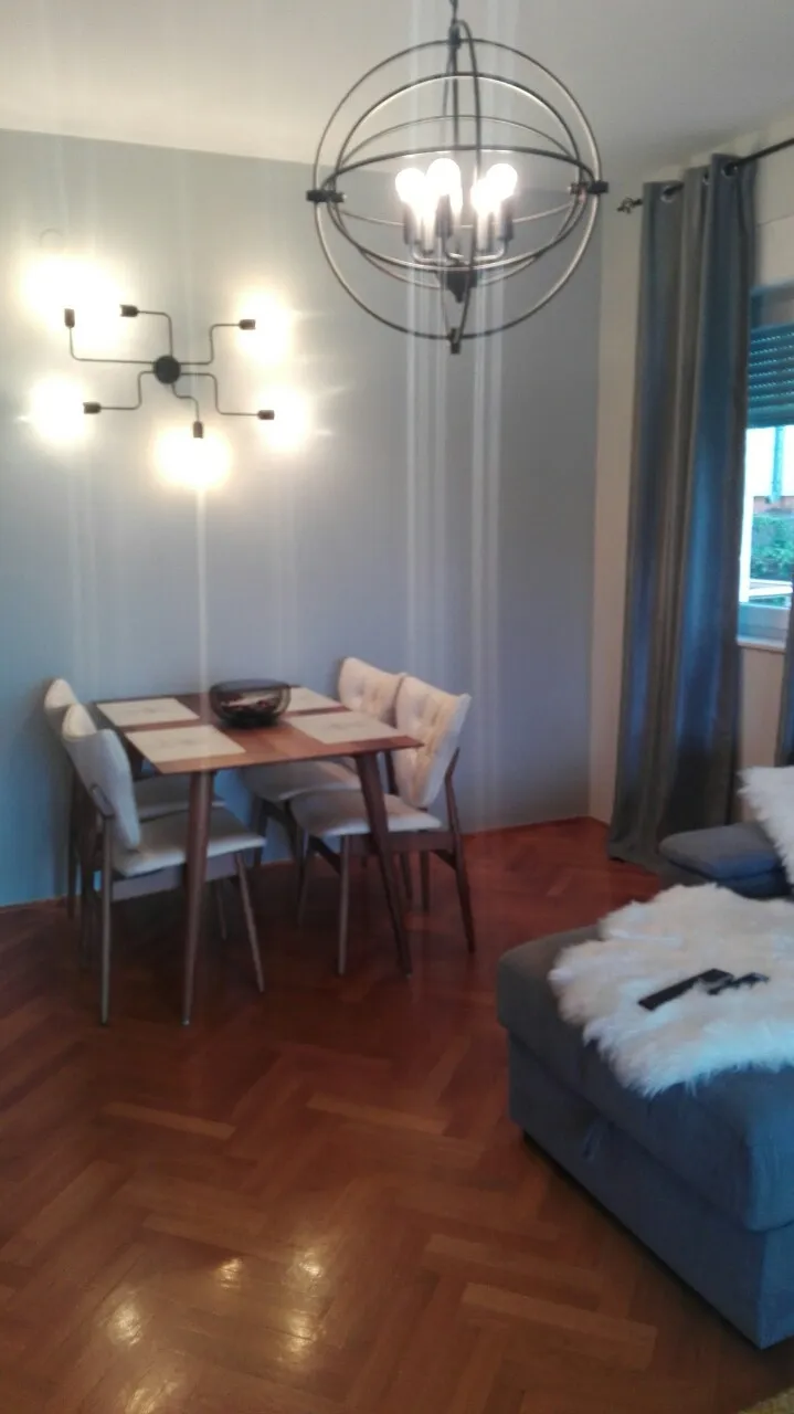 Wohnzimmerinterieur mit Esstisch, modernem Kronleuchter, Wandleuchte und Sofa.