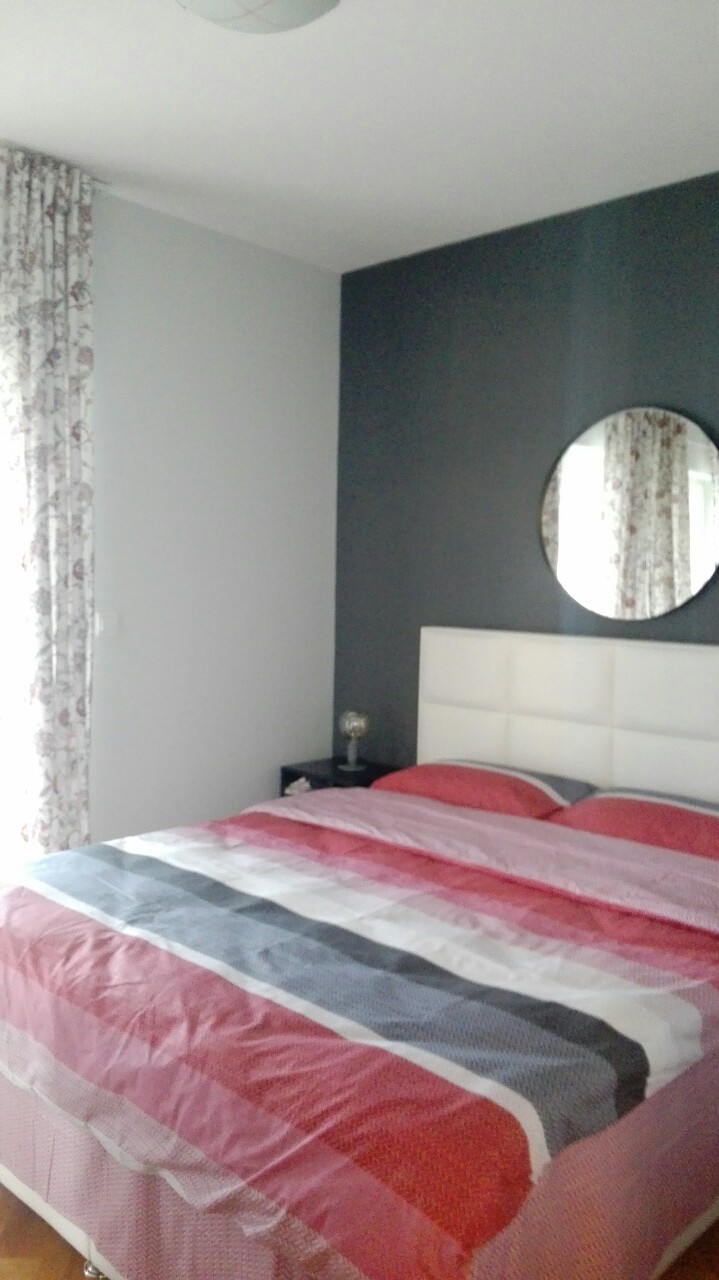 Schlafzimmer in einer Wohnung in Herceg Novi, Montenegro: Doppelbett mit weißem Kopfteil, Akzentwand und runder Spiegel.